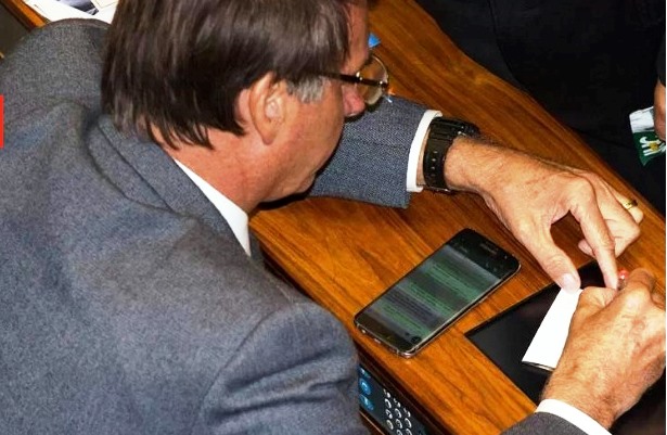 Bolsonaro lê conversas no WhatsApp em celular sentado na bancada do plenário da Câmara dos Deputados (Foto: Lula Marques/ Divulgação – Metrópoles)